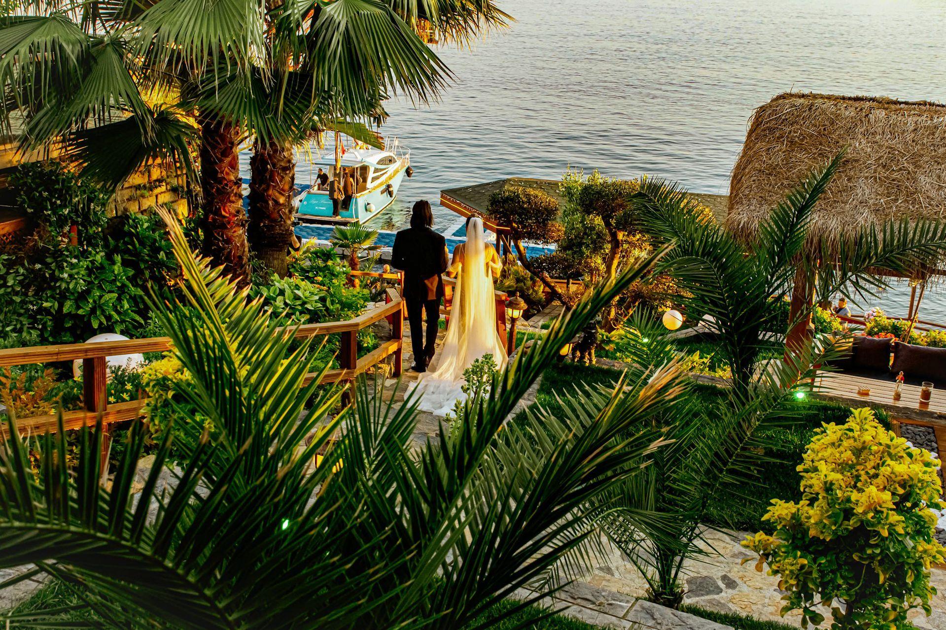 Sedef Adası’nda deniz kıyısına ve tekneye doğru yürüyen gelin ve damat ile ada düğünü atmosferi
